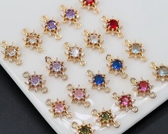 May include: A collection of gold-colored jewelry charms with colorful gemstone centers. Each charm features a starburst design around the central stone, with small clear crystals and loops for attachment. The gemstones are various colors.