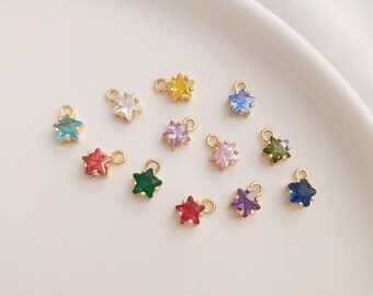 May include: Assortment of gold star charms with colorful crystal accents. The charms are arranged on a white surface.