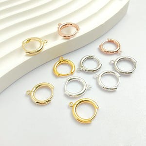 Könnte beinhalten: Eine Sammlung von Creolen-Verschlüssen in Gold, Roségold und Silber. Die Verschlüsse sind rund mit einer kleinen Schlaufe zum Befestigen des Ohrrings. Die Verschlüsse werden auf einer weißen Oberfläche präsentiert.