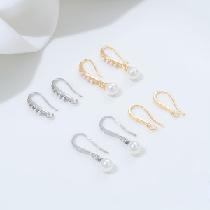 May include: An assortment of earrings in gold and silver tones, featuring pearl and rhinestone accents. The earrings include various styles, such as drop earrings and ear wires, suitable for jewelry making or personal wear. The pearls are white and the rhinestones are clear.