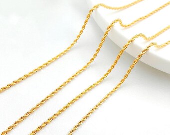 May include: Close-up of several gold-colored rope chains. The chains are arranged diagonally across the frame, with a bright, reflective surface. The chains have a twisted design, and the background is a soft white.