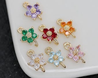 May include: A collection of colorful flower-shaped charms. Each charm features a gold-colored base with a flower design made of various colored gemstones, including purple, green, red, orange, white, blue, and pink. The charms have a small loop for attaching to jewelry.