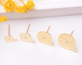 May include: Gold-colored earring posts in various sizes, featuring a flat, oval-shaped base with a loop for attaching charms or other decorative elements. The posts are designed for jewelry making and are displayed on a white surface with yellow flowers.