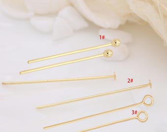 May include: Close-up of several gold-colored head pins for jewelry making. The pins have different head styles, including ball, flat disc, and looped. The pins are arranged on a soft, white background.