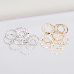 Könnte beinhalten: Nahaufnahme von zwei Gruppen dünner Ringe, einer silbernen und einer goldenen. Die Ringe sind in kleinen Gruppen angeordnet, vor einem schlichten, cremefarbenen Hintergrund. Die Kreise sind schlicht.