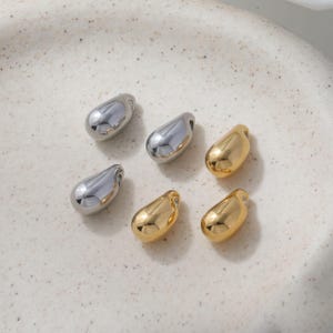May include: A collection of six small, smooth, teardrop-shaped charms. Three of the charms have a polished silver-tone finish, and three have a polished gold-tone finish. Each charm features a small hole at the top for attachment purposes.