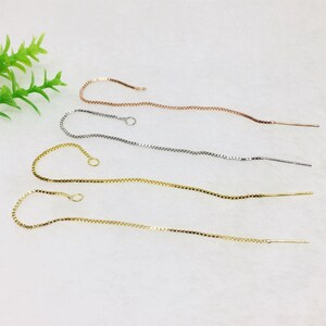 May include: Four threader earrings in gold, silver, and rose gold tones. Each earring features a delicate chain with a small loop at one end and a thin, straight post at the other. The earrings are displayed on a white surface.