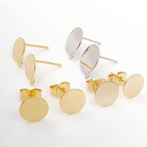 May include: A collection of gold and silver-colored earring posts and backs. The posts have a flat, round design, with some featuring a loop for attaching charms. The backs are butterfly style.