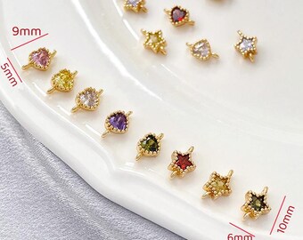 May include: A collection of gold-colored jewelry findings, including heart and star shapes, each with a colorful gemstone. The heart-shaped findings measure 5mm x 9mm, and the star-shaped findings measure 6mm x 10mm. The gemstones are in various colors.