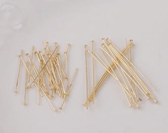 May include: A collection of gold-colored head pins, each with a small, flat disc at one end. The pins are scattered across a white surface, with some grouped together and others spread out. These pins are ideal for jewelry making and crafting.