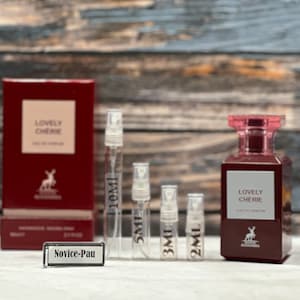 May include: A set of perfume samples in various sizes, including a 10 ml, 5 ml, 3 ml, and 2 ml bottle. The bottles are clear glass with a black cap. The perfume is called "Lovely Cherie" and is packaged in a red box with a white kangaroo logo. The text "Novice-Pau" is visible on a white label.