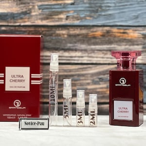 May include: A set of four perfume sample vials in different sizes, labeled 2ml, 3ml, 5ml, and 10ml. The vials are next to a red box with the text "Ultra Cherry Eau de Parfum" and a larger bottle of the same perfume.