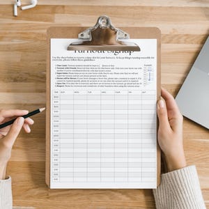 May include: A clipboard with a metal clip holds a white sheet titled "Turnout Signup." The sheet has a grid for time slots and days of the week. A pencil and a laptop are also visible on the wooden surface.