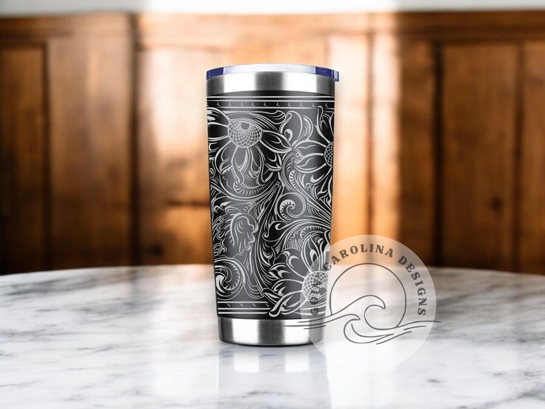 Peut inclure: Un gobelet en acier inoxydable noir et blanc avec un motif floral. Le gobelet a un couvercle noir et un logo blanc qui dit "CAROLINA DESIGNS".