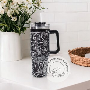 Peut inclure: Un gobelet en acier inoxydable noir et blanc avec un motif floral et un couvercle noir. Le gobelet a une poign&eacute;e et une paille.
