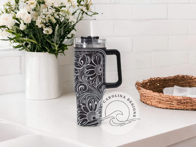 Peut inclure: Un gobelet en acier inoxydable noir et blanc avec un motif floral et un couvercle noir. Le gobelet a une poign&eacute;e et une paille.