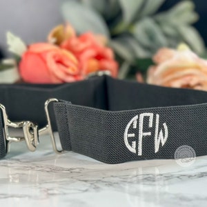 May include: A gray elastic belt with a silver buckle and a white monogram "EFW" embroidered on the front.