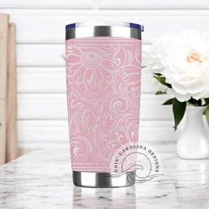 Peut inclure: Un gobelet isotherme en acier inoxydable rose avec un motif floral blanc. Le gobelet a un couvercle noir et un logo blanc qui dit "Goin' Carolina Designs".