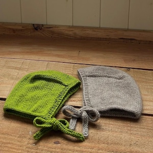 May include: Two knitted bonnets, one in a vibrant lime green and the other in a soft heather gray. Each bonnet features a structured brim, a smooth stockinette stitch pattern, and matching knitted chin straps that tie into a bow at the front.