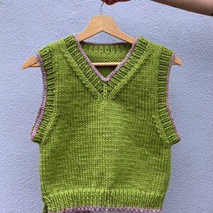 Puede incluir: Un chaleco de punto verde sin mangas con ribete rosa alrededor del cuello y las sisas.