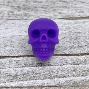 Peut inclure: Une petite figurine de cr&acirc;ne de couleur violette. Le cr&acirc;ne a un visage d&eacute;taill&eacute; avec des orbites, un nez et une bouche.