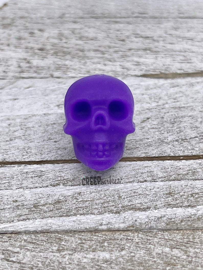 Peut inclure: Une petite figurine de cr&acirc;ne de couleur violette. Le cr&acirc;ne a un visage d&eacute;taill&eacute; avec des orbites, un nez et une bouche.
