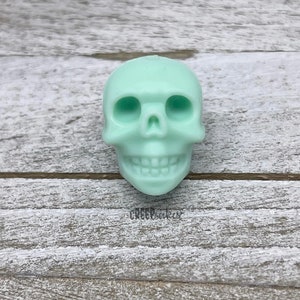 Peut inclure: Un petit cr&acirc;ne en r&eacute;sine de couleur vert clair. Le cr&acirc;ne a un visage d&eacute;taill&eacute; avec des orbites, un nez et une bouche avec des dents.