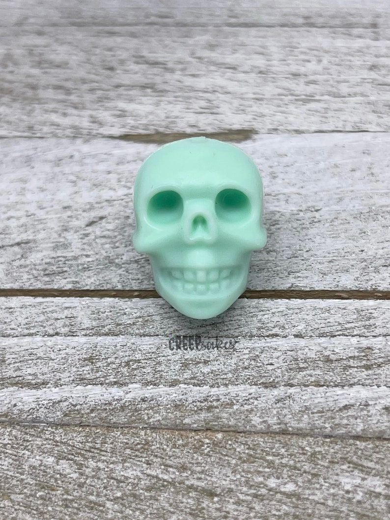 Peut inclure: Un petit cr&acirc;ne en r&eacute;sine de couleur vert clair. Le cr&acirc;ne a un visage d&eacute;taill&eacute; avec des orbites, un nez et une bouche avec des dents.