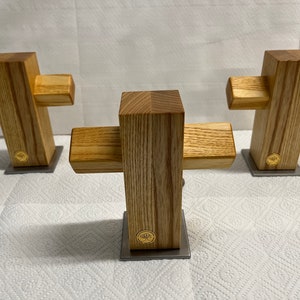 Könnte beinhalten: Drei Holzkreuze mit einer natürlichen Holzmaserung. Jedes Kreuz ist auf einem kleinen silbernen quadratischen Sockel montiert.
