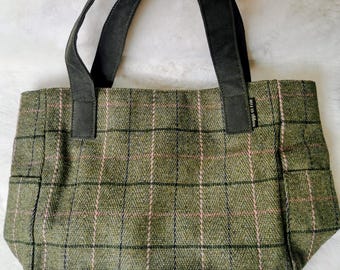 May include: A tote bag made of green textured fabric with a black and pink plaid pattern. The bag features two black fabric handles and a small black tag on the right side with the white text "Loggs of Fife" printed vertically on the label.