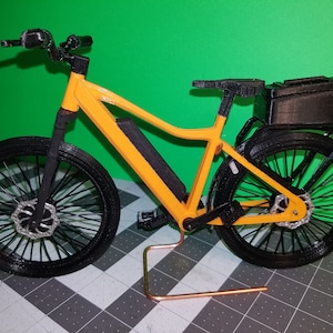 May include: A 3D printed model of a yellow electric bicycle with black wheels, a black seat, and a black cargo box on the back.