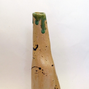May include: A handmade ceramic vase with a beige body and a green-glazed rim. The vase has a unique, asymmetrical shape with dark blue and brown speckles and accents. The vase is approximately 25 cm tall.