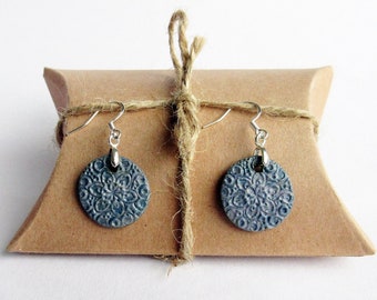 Può includere: Un paio di orecchini blu e argento con un delicato motivo floreale. Gli orecchini sono esposti in una scatola di carta marrone.