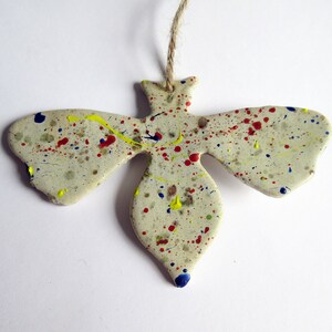May include: A ceramic bee ornament with a white base and colorful paint splatters in red, yellow, and blue.