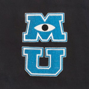May include: Blue and white embroidered patch with the letters "MU" and a white eye with a black pupil in the centre of the "M".