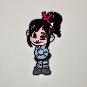 May include: An embroidered patch featuring a cartoon character with black hair tied in a high ponytail with a red ribbon, wearing a light blue hooded sweatshirt, a dark brown skirt, and striped leggings with grey boots, accented with colorful sprinkles.