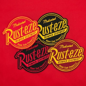 May include: Three embroidered patches with the text "Medicated Rusteze Bumper Ointment Rear End Formula" in yellow and red lettering on a black, red, and maroon background.