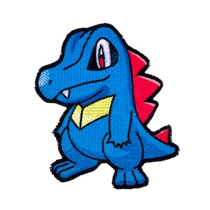 May include: Embroidered patch featuring a blue cartoon crocodile-like creature with red spikes on its back and a yellow chest. The creature has white teeth, a white eye, and a black outline. The patch is on a white background.