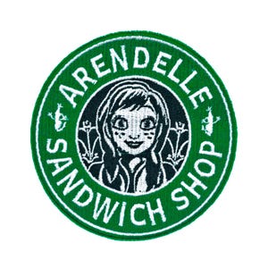 May include: A circular embroidered patch featuring a green border with the white text ARENDELLE SANDWICH SHOP. The center displays a black and white illustration of a character with braided hair, flanked by two small floral icons on each side.