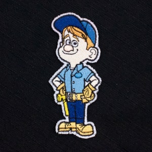 Könnte beinhalten: Gestickter Aufnäher mit einer Comicfigur, die eine blaue Mütze, ein blaues Hemd und eine gelbe Hose trägt. Die Figur hält ein gelbes Werkzeug in der rechten Hand und ein gelbes Werkzeug in der linken Hand. Die Figur hat ein weißes Gesicht mit einem Lächeln und braune Haare.