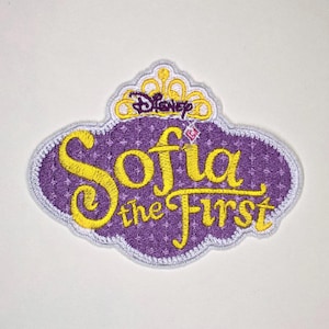 Könnte beinhalten: Ein gestickter Aufnäher mit dem violett-gelben Disney Sofia the First Logo. Das Design umfasst eine gelbe Krone an der Oberseite, einen violetten Hintergrund mit einem dezenten Rautenmuster und den Schriftzug Sofia the First in Gelb.