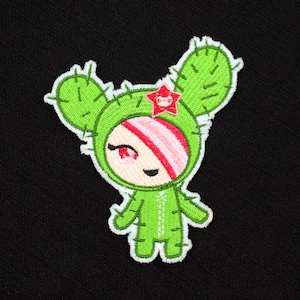 May include: Green cactus character with a pink and white striped hood and a red flower on top. The character has a smiling face with red eyes and a white outline.