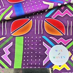 May include: Purple fabric with a vibrant geometric pattern. The design includes leaf-like shapes in red and orange, zigzags, and stripes in green, blue, and pink. White polka dots and vertical lines add detail. A circular sticker reads "WAX & WOVEN".