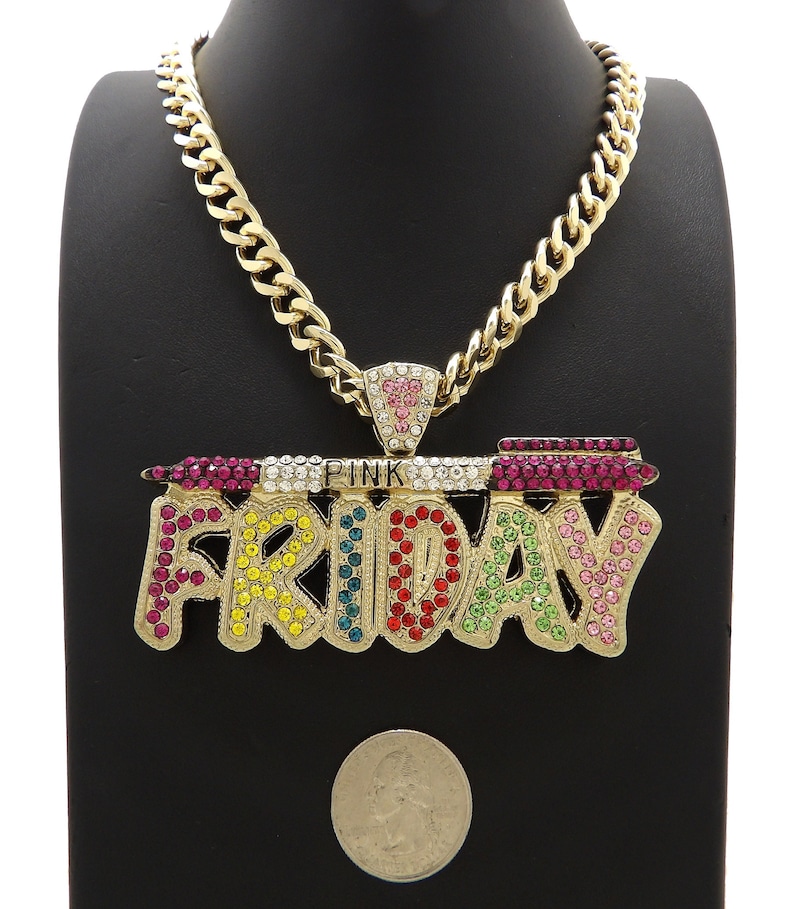 May include: Gold chain necklace with a large pendant that says "PINK FRIDAY" in colourful rhinestones. The pendant is shaped like a banner with a small pink heart at the top.