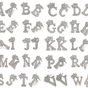 May include: A set of silver-toned earrings featuring the letters of the alphabet, each letter topped with a crown of sparkling rhinestones.