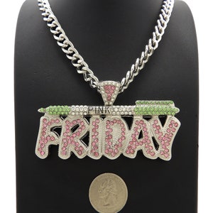 May include: A silver chain necklace with a large pendant that says "PINK FRIDAY" in pink and green rhinestones. The pendant is surrounded by smaller clear rhinestones.