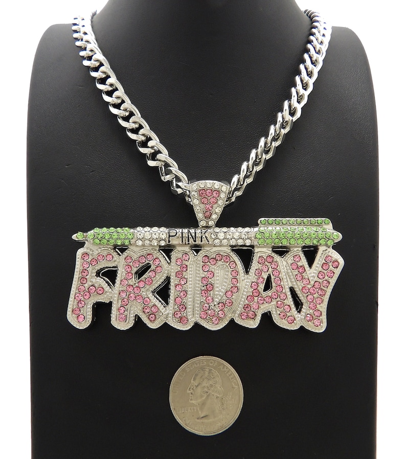May include: A silver chain necklace with a large pendant that says "PINK FRIDAY" in pink and green rhinestones. The pendant is surrounded by smaller clear rhinestones.