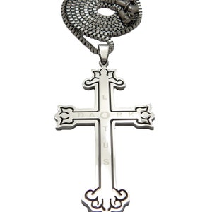 May include: A silver chain necklace with a silver cross pendant. The cross has a detailed design and the words "LA ORK DAOTUS" engraved on it.
