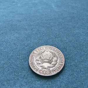 May include: A silver coin with the text "ПРОЛЕТАРИИ ВСЕХ СТРАН, СОЕДИНЯЙТЕСЬ!" and the text "СССР 1959" around a globe with a star on top.