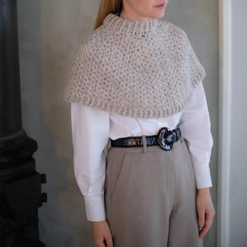 May include: A light gray knitted cowl neck collar with a white shirt and a black belt with a large buckle.